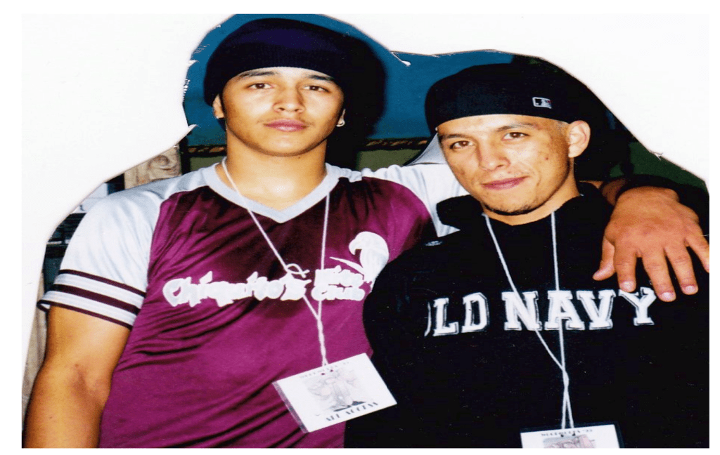 Two men, one with his arm around the other's shoulder, wearing caps and name tags on lanyards.