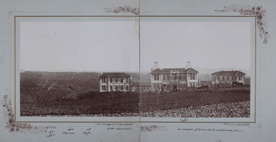 A black and white image framed with a floral design showing three two-story buildings with horses in front of them and empty lands all around.  